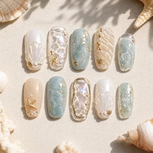 Puede incluir: Diez u&ntilde;as postizas con tem&aacute;tica playera. Los dise&ntilde;os incluyen conchas marinas, estrellas de mar, perlas y detalles dorados. Los colores son blanco, azul, beige y dorado, creando una est&eacute;tica costera.