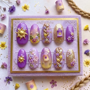 May include: A set of ten purple press-on nails with gold accents. Designs include a sun, a lantern, floral braids, and glitter. The nails are arranged on a lavender background with decorative elements.
