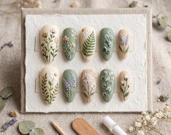 Puede incluir: Un juego de diez uñas postizas en forma de almendra con diseños botánicos en relieve 3D. Las uñas están pintadas en tonos crema y verde salvia, decoradas con flores, helechos, ramas de lavanda y hojas de eucalipto pintadas a mano.
