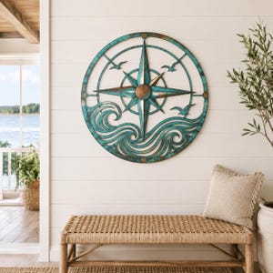 May include: A circular metal wall art piece featuring a central compass rose design with a weathered teal and copper finish. The lower portion depicts stylized ocean waves, while three small bird silhouettes are positioned above the waves.