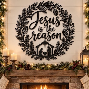 May include: A black metal wall sign featuring a circular wreath design made of pine branches, pinecones, and berries. The center text reads "Jesus is the reason" in a script font, positioned above a silhouette of a nativity scene with a star.