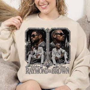 May include: A beige crewneck sweatshirt featuring a graphic print of Usher and Chris Brown. The design includes two framed portraits of the artists in suits and sunglasses, with the text Usher Raymond & Brown printed in a glittery, silver-toned font.