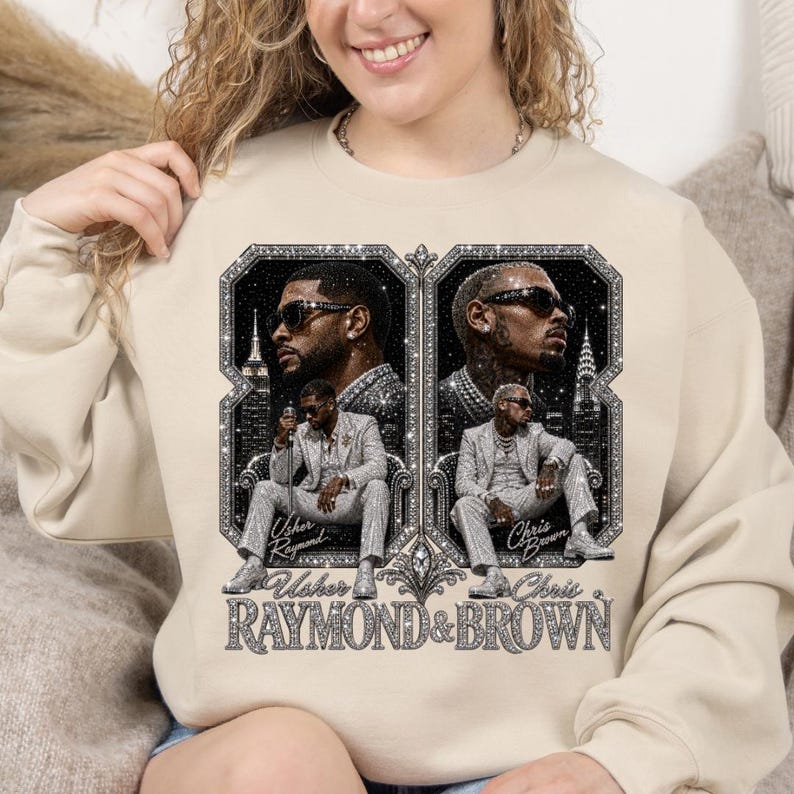 May include: A beige crewneck sweatshirt featuring a graphic print of Usher and Chris Brown. The design includes two framed portraits of the artists in suits and sunglasses, with the text Usher Raymond & Brown printed in a glittery, silver-toned font.