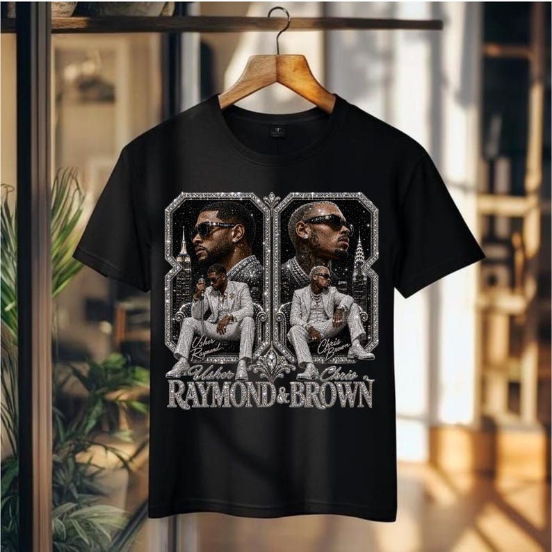 May include: A black short-sleeve t-shirt featuring a graphic print of Usher and Chris Brown. The design includes two framed portraits of the artists in suits, set against a city skyline background with the text Usher Raymond & Brown below.