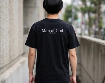 May include: Black t-shirt with the text "Man of God" and "1 Timothy 6:11" printed in white. The shirt is a classic crew neck style.