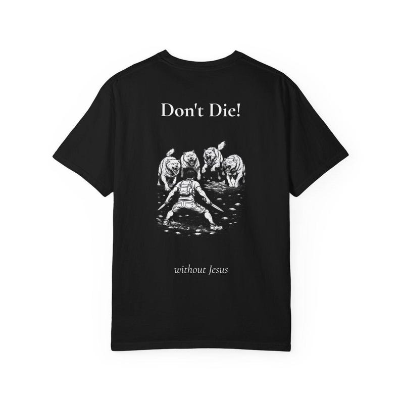 Op de afbeelding: Zwart t-shirt met een witte afbeelding van een persoon die vier dieren confronteert. De tekst "Don't Die!" staat boven de illustratie, met "without Jesus" eronder.