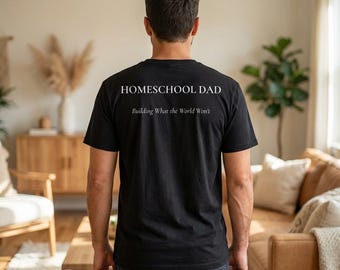 Puede incluir: Camiseta negra con el texto "HOMESCHOOL DAD" encima de "Building What the World Won't" en blanco. La camiseta la lleva una persona, vista por la espalda, en una habitación bien iluminada con un sofá y muebles de madera.