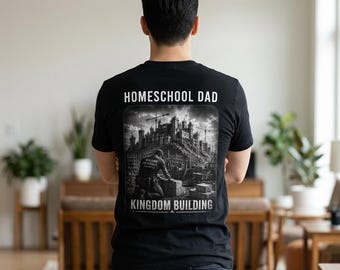 Puede incluir: Camiseta negra con el texto "HOMESCHOOL DAD" sobre un gráfico en escala de grises de una obra. El gráfico incluye una persona trabajando y las palabras "KINGDOM BUILDING" debajo.