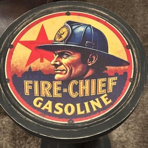 May include: A round, black-rimmed sign featuring a graphic of a firefighter in a blue helmet. The background displays a red star and a cityscape silhouette. The text reads FIRE-CHIEF GASOLINE in yellow letters against a dark blue and red circular backdrop.