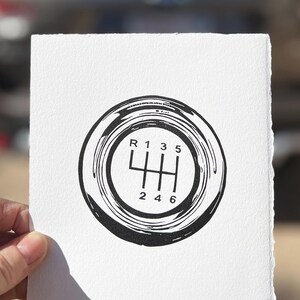 May include: Black and white illustration of a car's gear shift pattern. The pattern shows the positions for reverse, first, second, third, fourth, fifth, and sixth gear.