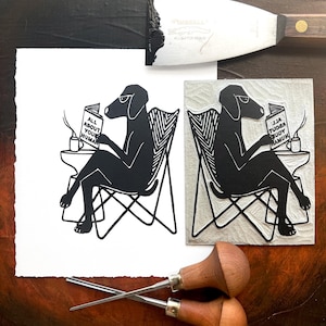 GUIDEBOOK, Dog Reading How To Book on Humans, Linocut Relief Print, Inktober 2024, Pup with Coffee in Modern Chair Reading