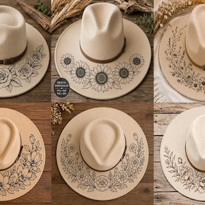 Könnte beinhalten: Eine Auswahl beiger Fedora-Hüte mit floralen Designs. Jeder Hut hat ein braunes Lederband und schwarze Blumenmuster, darunter Rosen und Sonnenblumen. Die Hüte werden auf einer Holzoberfläche präsentiert. Der Text „DIGITALER DOWNLOAD“ ist ebenfalls sichtbar.