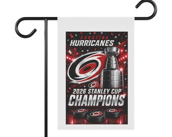 May include: A rectangular garden flag featuring the Carolina Hurricanes logo, a silver Stanley Cup trophy, and three hockey pucks. The text reads Carolina Hurricanes 2026 Stanley Cup Champions against a red and black background with confetti.