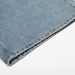 Peut inclure: Un gros plan sur l'ourlet d'un jean en denim bleu clair. Le tissu pr&eacute;sente une texture en serg&eacute; classique avec des coutures visibles le long du bord inf&eacute;rieur, mettant en valeur la coupe droite et la construction durable du mat&eacute;riau en denim.