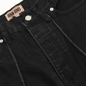 May include: Black denim jeans featuring a tan leather brand patch on the waistband with the text DENIM GENES, a silver metal button closure, and a tan leather pocket accent with a black star and letter C graphic, accented by white stitching.