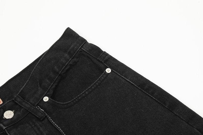 May include: A pair of black denim jeans featuring a classic five-pocket design with a structured waistband, a metal button closure, and silver-toned metal rivets reinforcing the pocket corners, showcasing a durable fabric texture and stitching.