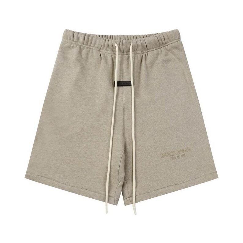 May include: Light heather gray sweat shorts featuring an elasticized waistband with long, off-white drawstring cords. A small black rectangular patch is centered below the waistband, and the word ESSENTIALS is embossed on the lower left leg.
