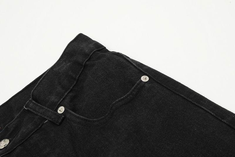 May include: A pair of black denim jeans featuring a classic five-pocket design, a high waistband with belt loops, and silver-toned metal rivets reinforcing the pocket corners. The fabric has a visible twill texture and sturdy stitching throughout.