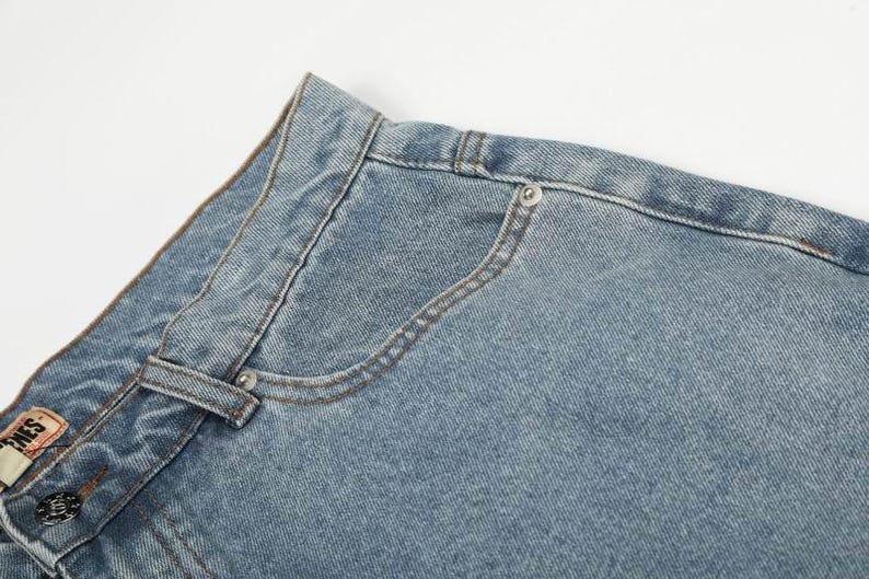 Peut inclure: Un jean en denim bleu clair dot&eacute; d'une coupe classique &agrave; cinq poches, d'une fermeture &agrave; bouton m&eacute;tallique, d'une petite poche gousset et de coutures apparentes. La ceinture comporte des passants et une &eacute;tiquette de marque rectangulaire.