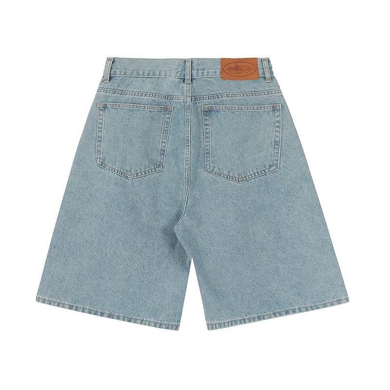May include: Light blue denim shorts featuring a high-waisted design with a tan leather patch on the back waistband. The shorts include two back pockets, belt loops, and a classic button and zipper fly closure with visible stitching throughout.