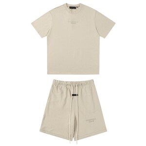 May include: A beige short-sleeve t-shirt and matching shorts set. The t-shirt features a crew neckline and subtle text on the chest. The shorts have an elastic waistband with long white drawstrings and a small black rectangular label.