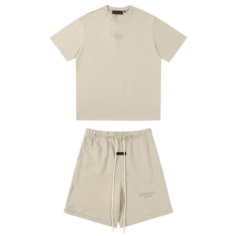 May include: A beige short-sleeve t-shirt and matching shorts set. The t-shirt features a crew neckline and subtle text on the chest. The shorts have an elastic waistband with long white drawstrings and a small black rectangular label.