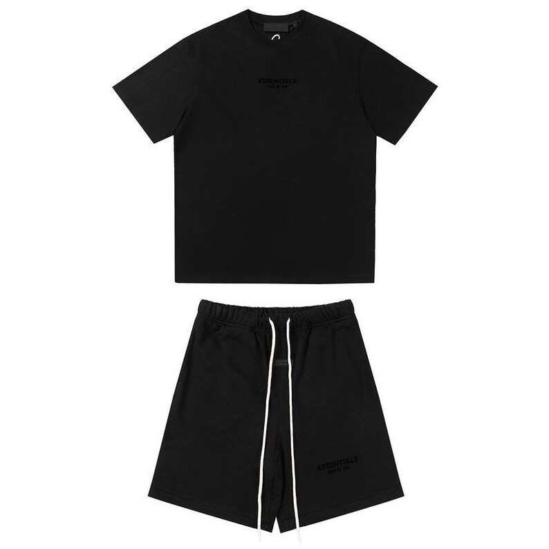 May include: A black short-sleeve t-shirt and matching black shorts set. The t-shirt features the word ESSENTIALS printed on the chest. The shorts have an elastic waistband with long white drawstrings and the word ESSENTIALS printed on the leg.