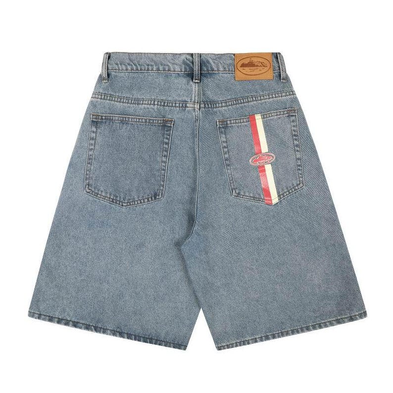 Peut inclure: Short en jean bleu clair avec une taille haute et une &eacute;tiquette en cuir marron sur la ceinture arri&egrave;re. La poche arri&egrave;re droite pr&eacute;sente une bande verticale rouge et blanche avec un petit &eacute;cusson ovale centr&eacute; sur la bande.