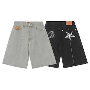 May include: Two pairs of denim shorts, one light gray and one black. The light gray pair features a tan leather patch on the front pocket. The black pair has a tan leather patch on the back waistband and white embroidered star designs on the pockets.