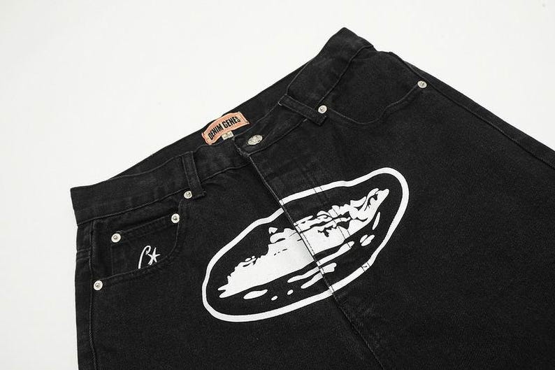 May include: Black denim jeans featuring a large white oval graphic print on the front. The waistband includes a tan label with the text DENIM GENES and silver-toned metal rivets. A small white star logo is embroidered on the front pocket area.