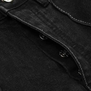 May include: A pair of black denim jeans featuring a button-fly closure with metallic silver buttons. The fabric has a visible twill texture and is accented with contrasting white stitching along the seams and the placket of the fly.