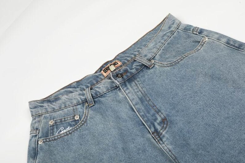 Peut inclure: Jean en denim bleu clair avec une taille haute, une fermeture &agrave; bouton et une braguette zipp&eacute;e. La ceinture comporte des passants et une petite &eacute;tiquette rectangulaire de marque Denim Bones. Une petite poche gousset pr&eacute;sente une broderie.