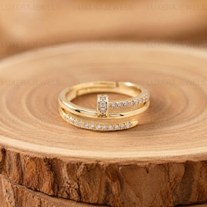 May include: A gold-toned ring featuring a bypass design with two open ends. The band is embellished with a row of small, clear, sparkling stones along the outer edge and a vertical bar set with similar stones connecting the two ends of the ring.