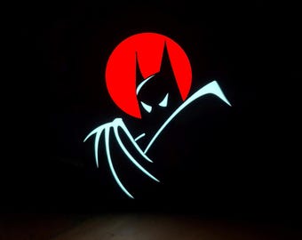 May include: A stylized Batman logo against a red circle, set against a black background. The Batman silhouette is white with a glowing effect, featuring pointed ears and a cape. The image evokes a comic book or animated style.