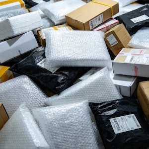 Könnte beinhalten: Ein Stapel verpackter Artikel, versandfertig. Die Pakete bestehen aus Kartons, schwarzen und weißen Poly-Versandtaschen und Luftpolsterfolie. Einige Kartons sind mit Klebeband oder gelben Bändern verschlossen. Die Artikel sind versandbereit.