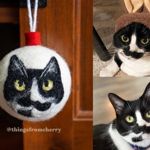 May include: A white felt ornament shaped like a cat's head with black and white fur and green eyes. The ornament is hanging from a red and white string. The text "@thingsfromcherry" is visible at the bottom of the image.