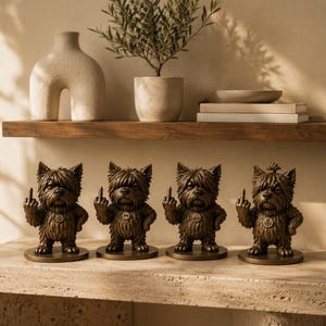 May include: Four bronze-coloured figurines of small, shaggy dogs standing on circular bases. Each dog has a textured coat, a collar with a circular tag, and is depicted with one paw raised, extending its middle finger in a gesture of defiance.