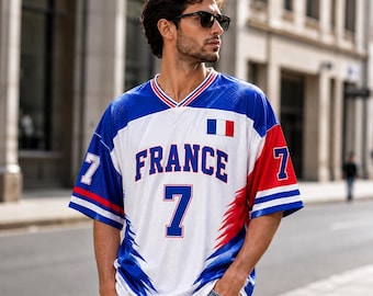 Puede incluir: Una camiseta de malla blanca, azul y roja con el texto FRANCE y el número 7 en la parte delantera. Las mangas muestran el número 7 y una pequeña bandera francesa está situada en el pecho. El diseño incluye detalles gráficos en azul y rojo.