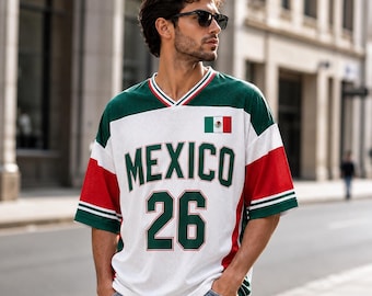 Puede incluir: Una camiseta de malla blanca, verde y roja con la palabra MEXICO en letras grandes verdes en el pecho, el número 26 en verde debajo y un pequeño emblema de la bandera mexicana en el lado derecho, con cuello en V y bordes a rayas.