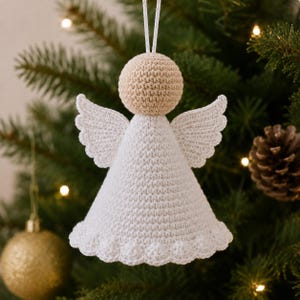 Op de afbeelding: Een gehaakte engelornament met een beige bolvormig hoofd en een wit kegelvormig lichaam met geschulpte randen. De engel heeft twee witte, getextureerde vleugels aan de zijkanten en een wit koordje aan de bovenkant om op te hangen.