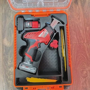 May include: A red and black cordless reciprocating saw with a battery pack, housed in an open orange plastic carrying case with custom-molded black foam inserts. The set includes multiple yellow saw blades stored in side slots.