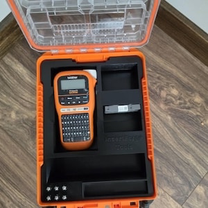 May include: An orange and black tool case with a clear lid. Inside, a Brother P-touch EDGE label maker is visible, along with storage compartments. The case is designed to protect and organize tools and accessories.