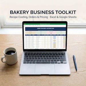 May include: A laptop displaying a Bakery Business Toolkit spreadsheet for recipe costing, orders, and pricing. The screen shows an Order Tracker and Revenue Log. A white ceramic mug filled with dark coffee and a blue pen sit on the desk.