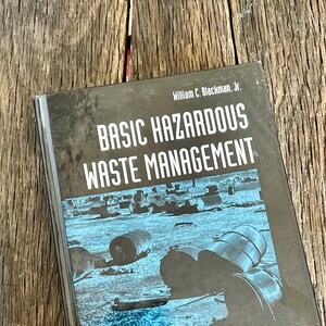 May include: A black book with the title "Basic Hazardous Waste Management" by William C. Blackman, Jr. The cover features a blue and white photo of barrels in a field.
