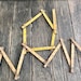 May include: A set of six yellow wooden folding rulers arranged in a house shape on a wooden surface. The rulers are marked with numbers from 1 to 37.