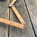 May include: A wooden folding ruler with markings in inches and feet. The ruler is made of light brown wood and has a worn, vintage look.