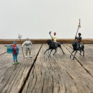May include: A collection of vintage toy soldiers and mounted figures. The figures include a soldier in blue and red, a knight in silver armor, and two mounted figures on black horses. The toys are arranged on a weathered wooden surface.