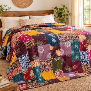 Op de afbeelding: Een patchwork sprei met een verscheidenheid aan rechthoekige stoffen panelen in tinten mosterdgeel, diepbordeaux, marineblauw, teal en magenta. De sprei toont diverse bloemrijke, geometrische en abstracte patronen met zichtbaar stikwerk.