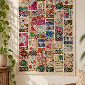 Op de afbeelding: Een rechthoekige wandhanger met een patchworkontwerp van diverse geborduurde stoffen vierkanten. Het textiel toont een levendige reeks bloemen-, paisley- en geometrische patronen in tinten roze, groen, blauw, oranje en goud.