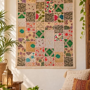 Könnte beinhalten: Ein rechteckiger Wandbehang mit einem Patchwork-Design, das aus zahlreichen quadratischen Stoffbahnen besteht. Jedes Feld zeigt unterschiedliche Stickmuster, florale Motive und geometrische Formen in verschiedenen Farben wie Grün, Rot, Gold und Grau, die durch sichtbare weiße Nähte verbunden sind.